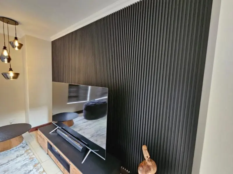 Charcoal slat panelling filling a living-room wall behind a wall-mounted TV and media unit